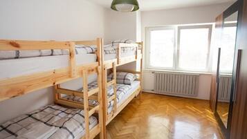 Quarto com beliche, piso de madeira, radiador e janela com persianas.