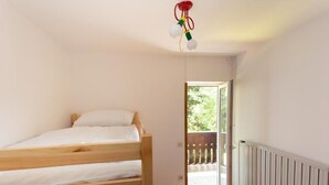 Een slaapkamer met een houten stapelbed, een witte radiator en een deur naar een buitenbalkon.