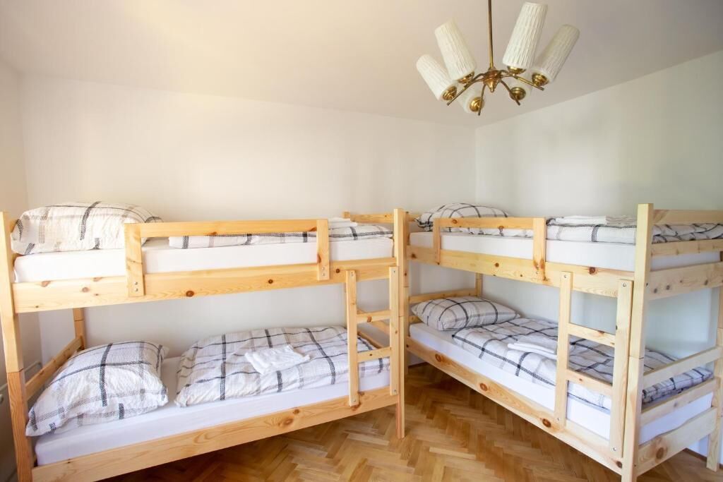 A room with four bunk beds, each with a plaid-patterned blanket and pillows. A chandelier hangs from the ceiling.