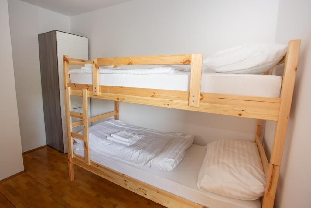 Una cama litera de dos plazas, un armario de madera y una cortina gris.