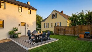 Un jardin avec une terrasse en bois, une table à manger avec des chaises et un barbecue.
