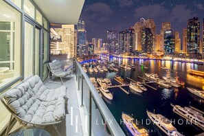 Ein Balkon mit gepolstertem Stuhl und Blick auf eine Marina mit Yachten und einem Stadtbild bei Nacht.