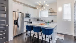 A modern kitchen with white cabinets, stainless steel appliances, a central island with blue bar stools, and a unique light fixture. - Rooftop Views Patio Lounge Near Downtown Nashville (Nashville)