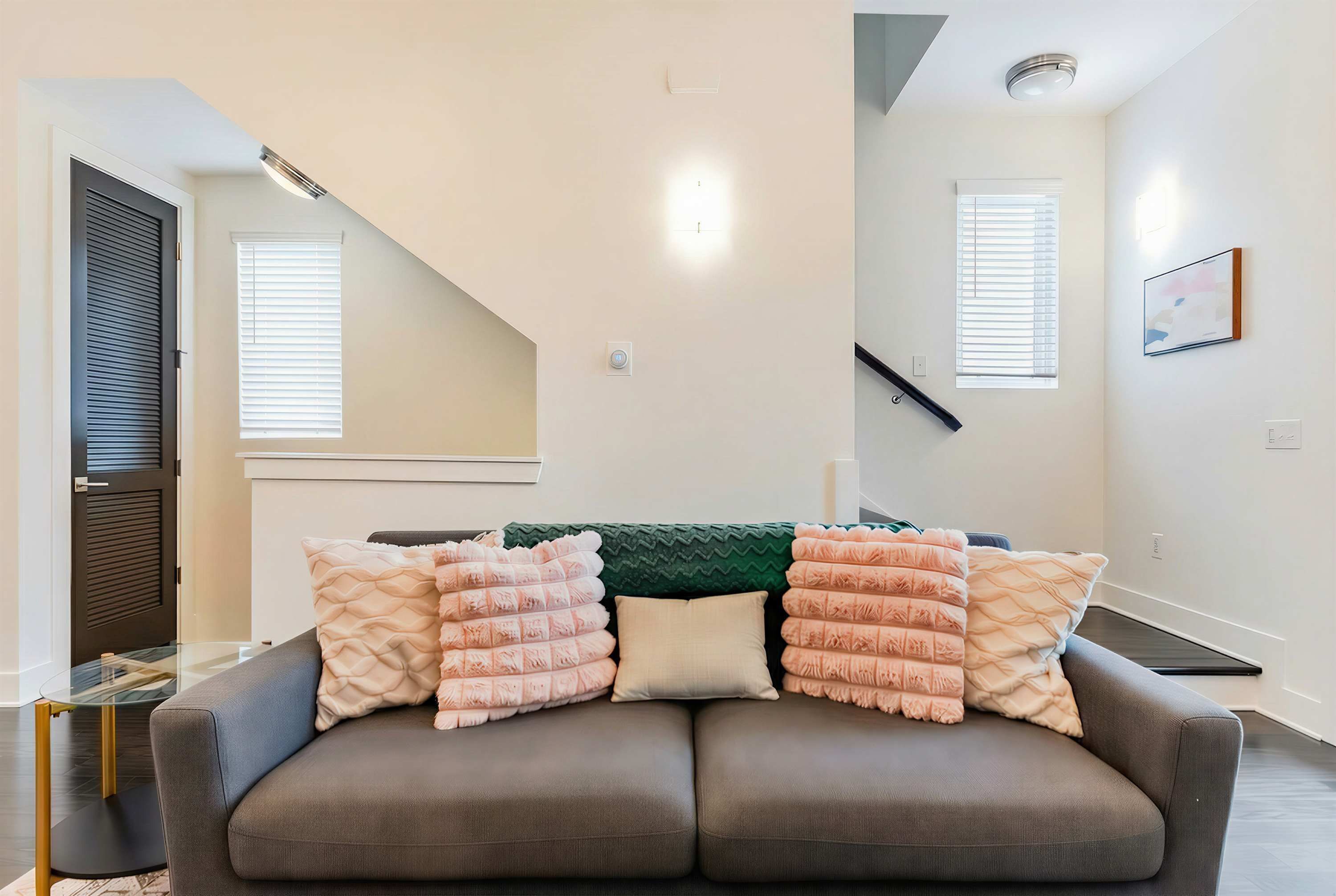 A modern living room with a grey sofa, multiple cushions, a green throw, and a glass coffee table.