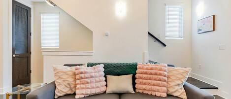 A modern living room with a grey sofa, multiple cushions, a green throw, and a glass coffee table.