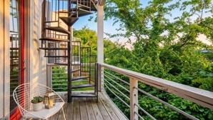 A wooden deck with a spiral staircase, a white chair with a potted plant, and a railing overlooking a lush garden. - Rooftop Views Patio Lounge Near Downtown Nashville (Nashville)