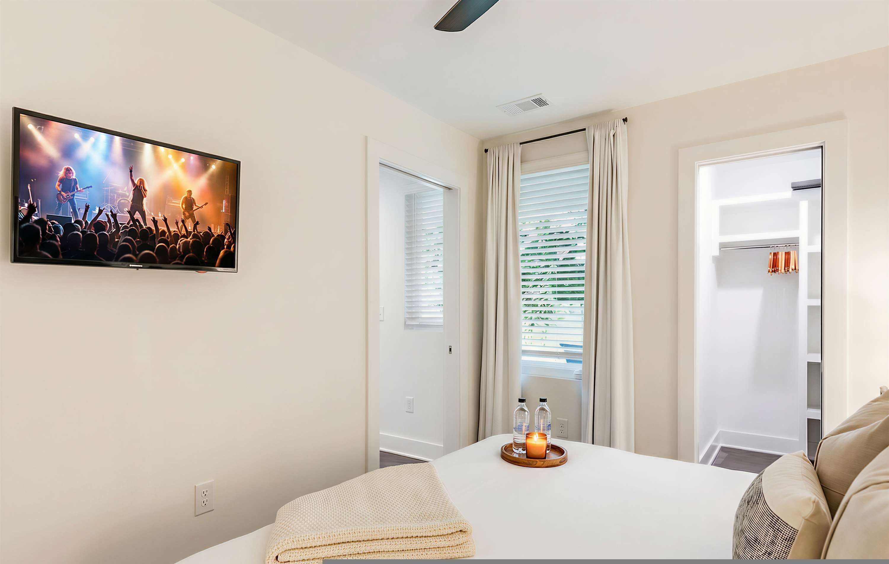 A hotel room with a bed, a TV on the wall, a window with curtains, and a closet.