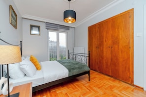 A bedroom with a bed, a wooden wardrobe, a window with a view, and a hanging light fixture.