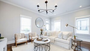 Una sala de estar moderna con un sofá blanco, dos sillones, una mesa de centro redonda y una araña.