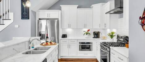 A modern kitchen with white cabinetry, stainless steel appliances, and a wooden floor.