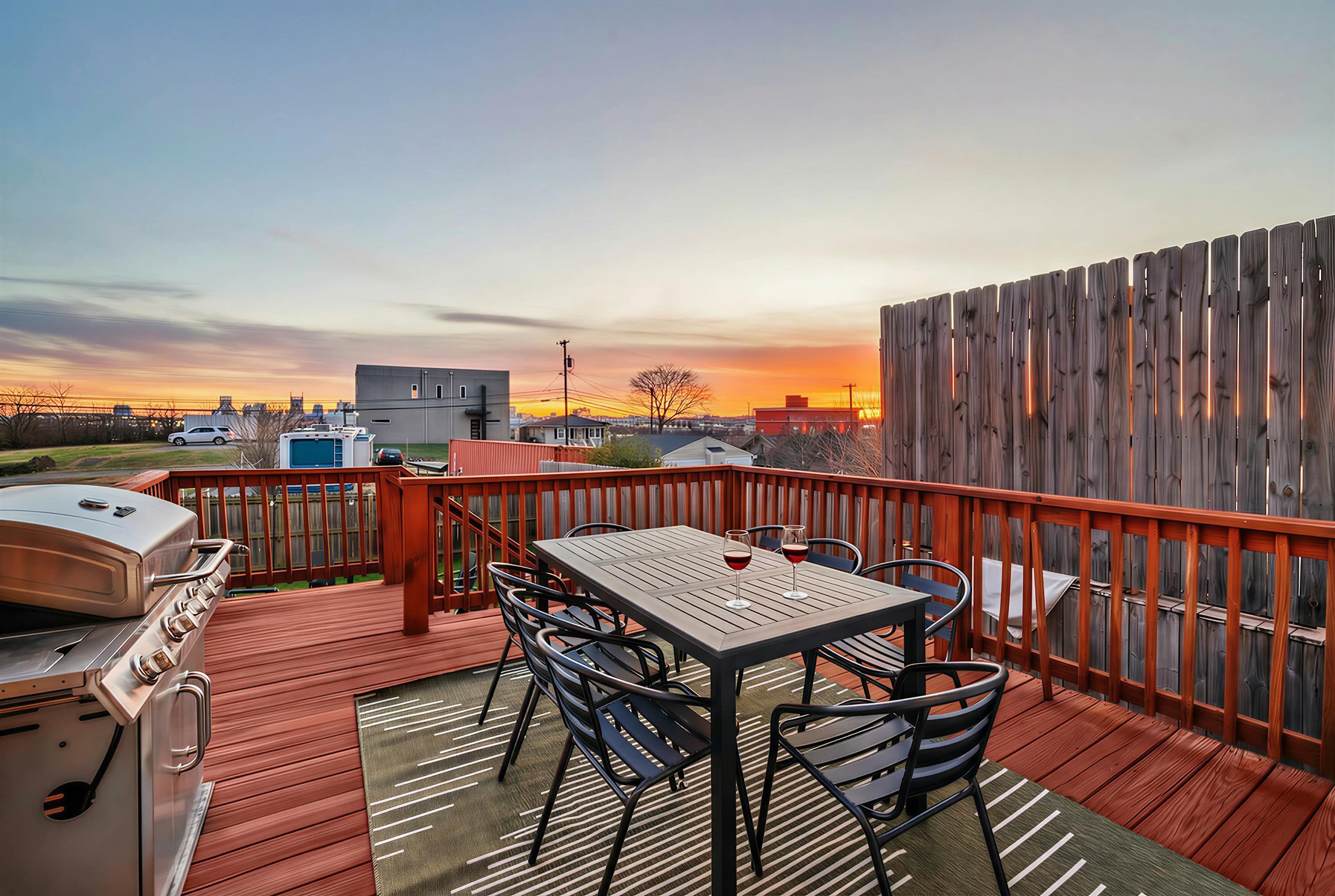 Terraza con parrilla, mesa y sillas, con vista a una puesta de sol.