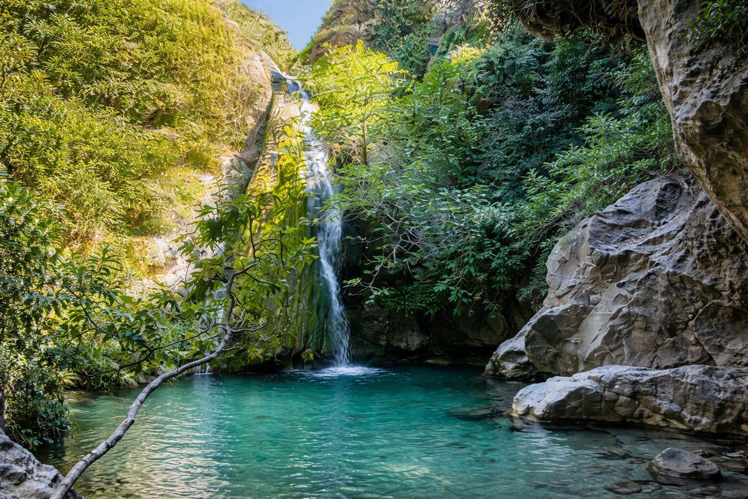 A waterfall cascading into a clear turquoise pool surrounded by lush greenery and rocky terrain.