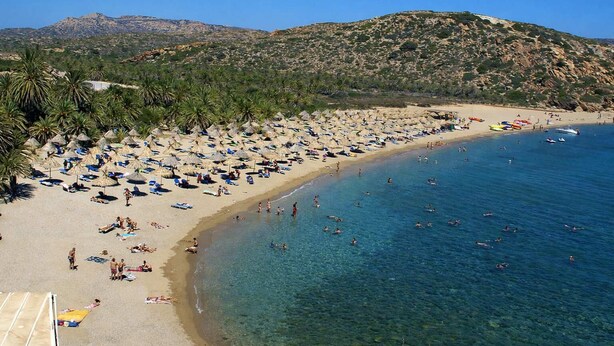 A beach with clear blue water, numerous umbrellas, and people enjoying the sun. - Sun Studio - Sitia Cozy Stay With Mountain Views (Sitia)
