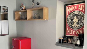 Ein kleiner Raum mit einem roten Kühlschrank, einer weißen Mülleiste und einem Regal mit Dekoration.