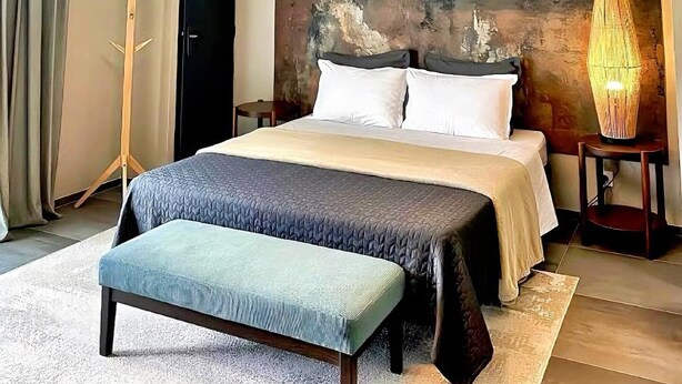 Ein modernes Schlafzimmer mit einem großen Bett, einer Bank, einem außergewöhnlichen Kopfteil und einer hängenden Leuchte.