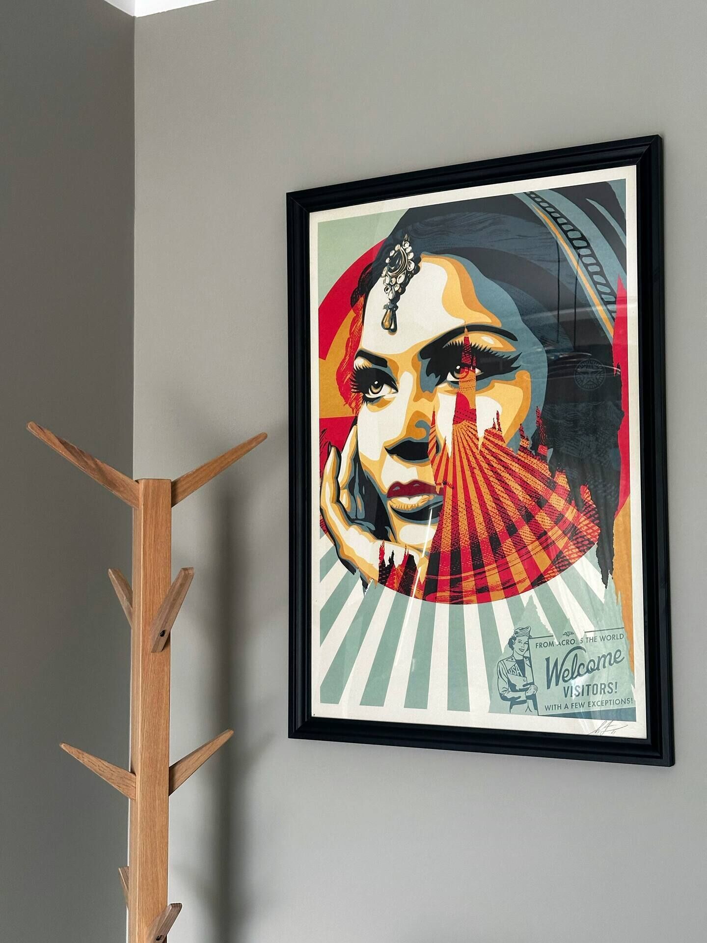 A framed artwork on a wall with a wooden coat rack beside it.
