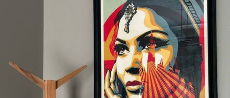 A framed artwork on a wall with a wooden coat rack beside it.