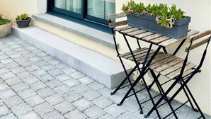 Ein modernes Gebäude mit einem großen Fenster, einer kleinen Außenbereich-Sitzgelegenheit mit Holztisch und -stühlen sowie Blumentöpfen.