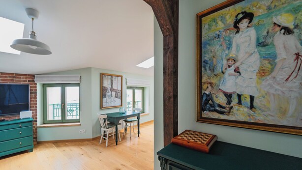 Ein geräumiges Zimmer mit Holzboden, einer Essecke mit Tisch und Stühlen, einem Fernseher an einer Ziegelwand und einem großen Gemälde an der Wand.
