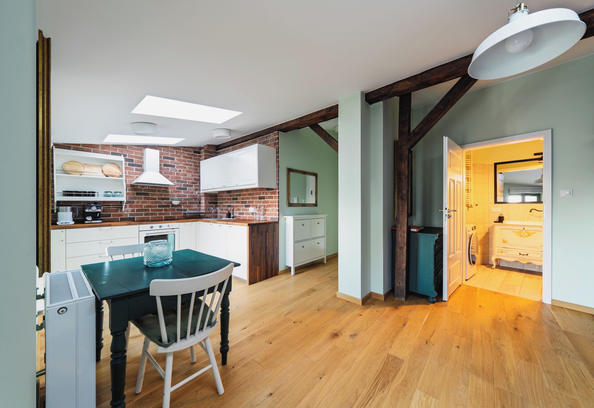A modern kitchen with a dining area, featuring a brick wall, white cabinets, and a wooden floor.