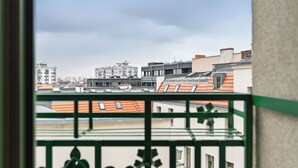 Blick von einem Balkon mit grüner Metallreling auf einen Stadtblick mit verschiedenen Gebäuden, darunter ein markantes weißes Gebäude mit der Nummer 17.