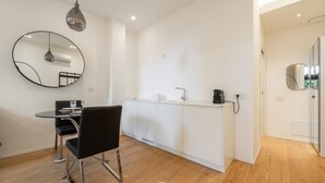 A modern kitchen with white cabinets, a round mirror, a dining table with chairs, and a hanging light fixture. - Loft 4 Via Campidano – Your city-centre retreat (Cagliari)