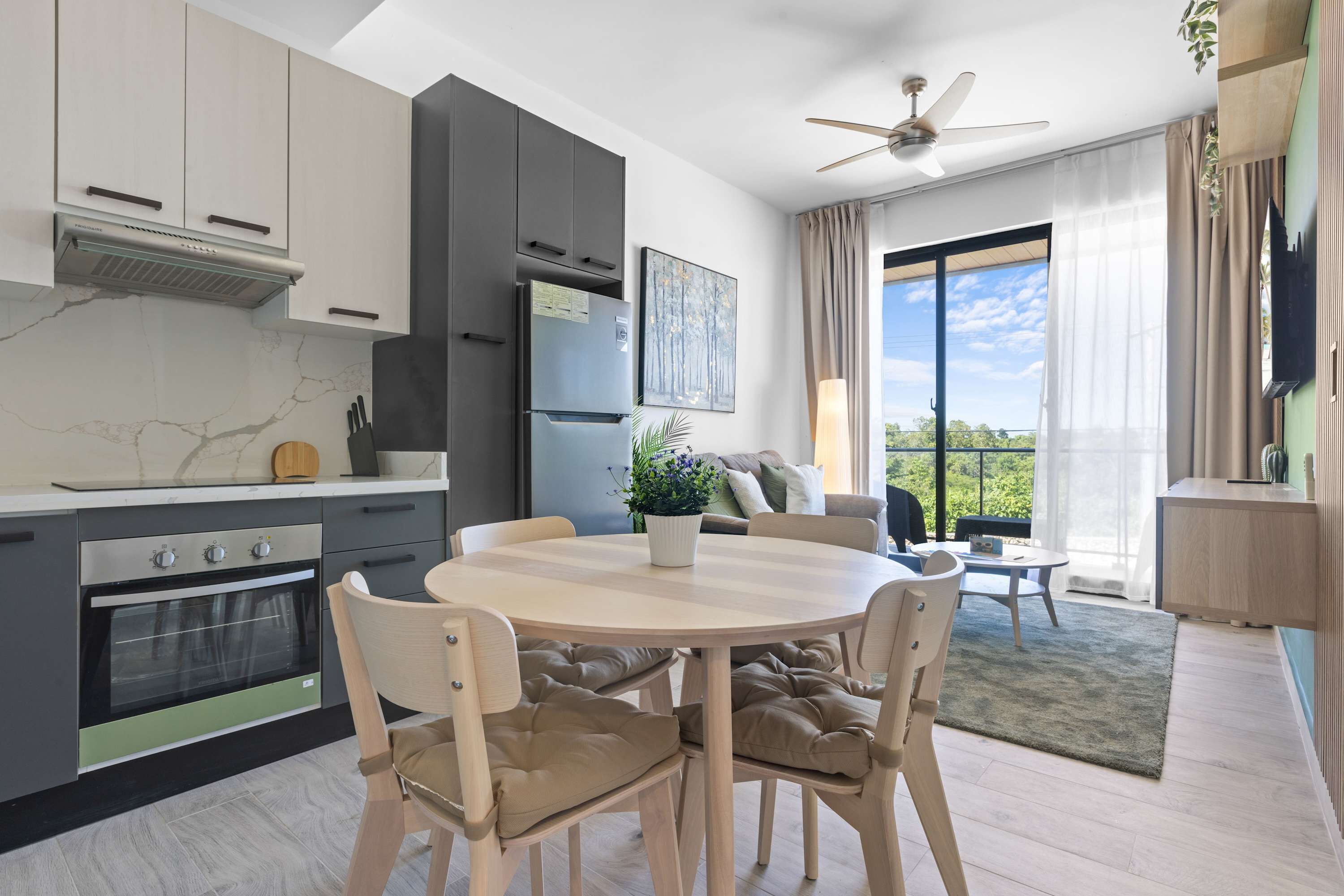 A modern kitchen with a dining area, a ceiling fan, and a view through large windows.