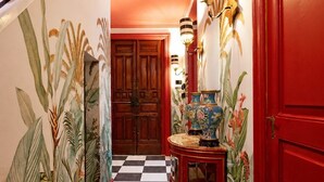 A hallway with a checkered floor, a wooden door, a red wall, and a wall-mounted light fixture. - Le Stanze di Monserrato (Catania)
