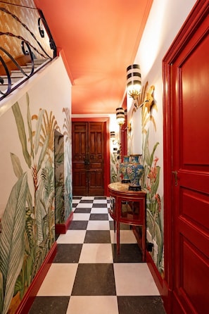 A hallway with a checkered floor, a wooden door, a red wall, and a wall-mounted light fixture. - Le Stanze di Monserrato (Catania)