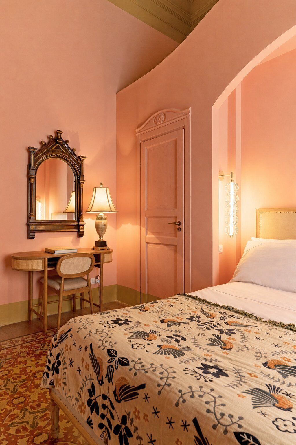 A bedroom with a bed, a desk with a chair, a door, and a mirror.