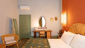 Ein Schlafzimmer mit einem Bett, einem Schreibtisch mit Spiegel, einem Sessel, einer Kommode und einer Tür.