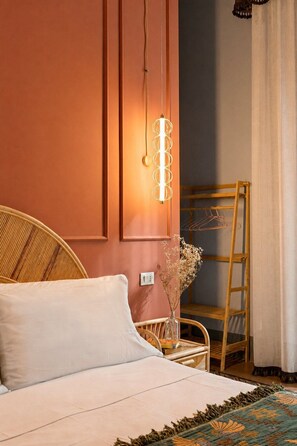 A bedroom with a bed, a wicker chair, a wooden ladder, a wall-mounted light fixture, and a vase with dried flowers. - Le Stanze di Monserrato (Catania)