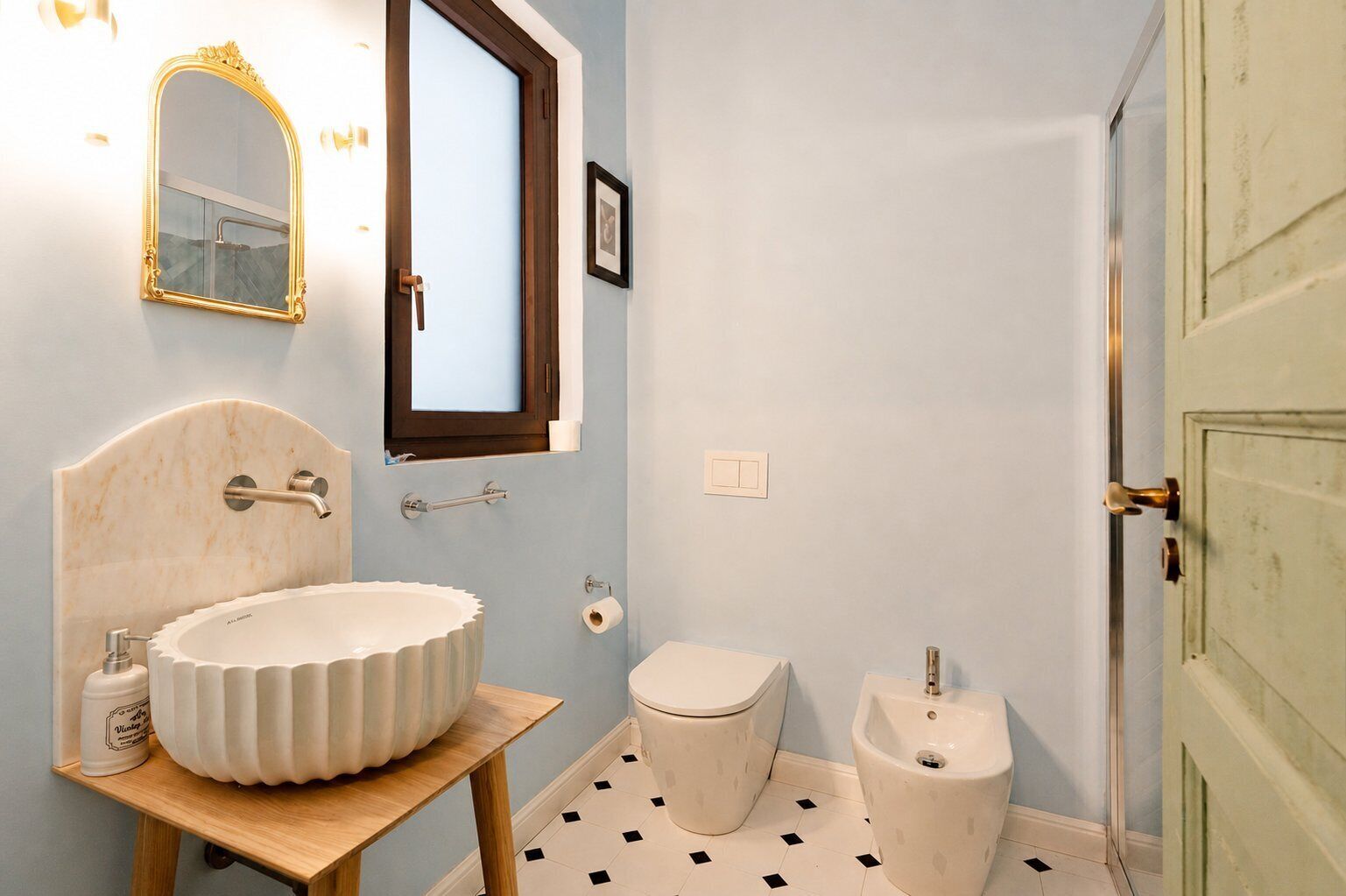 A bathroom with a marble sink, a toilet, a mirror, and a shower door.