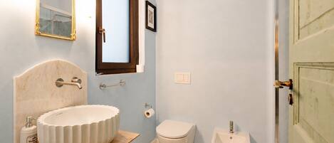 A bathroom with a marble sink, a toilet, a mirror, and a shower door.