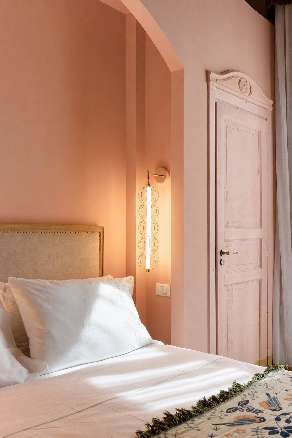 Une chambre à coucher avec un lit, un luminaire fixé au mur et une porte.