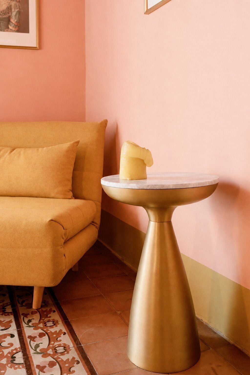A corner of a room with a sofa and a pedestal table with a candle.