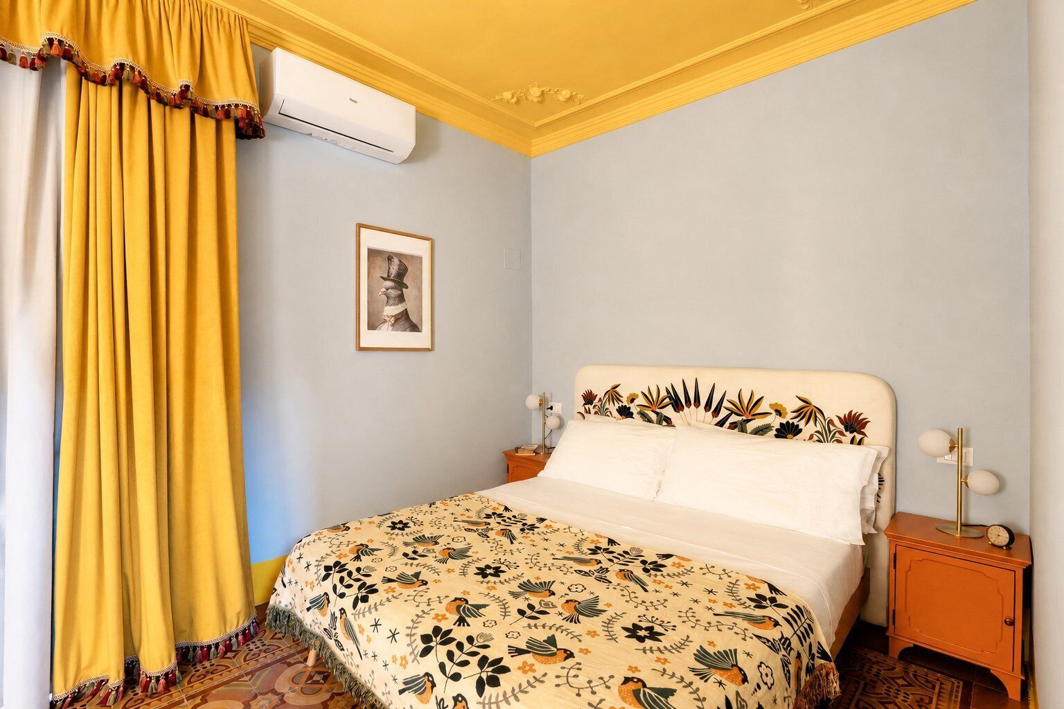 Een slaapkamer met een bed, nachtkastje, een wandairconditioner en een ingelijst beeld.