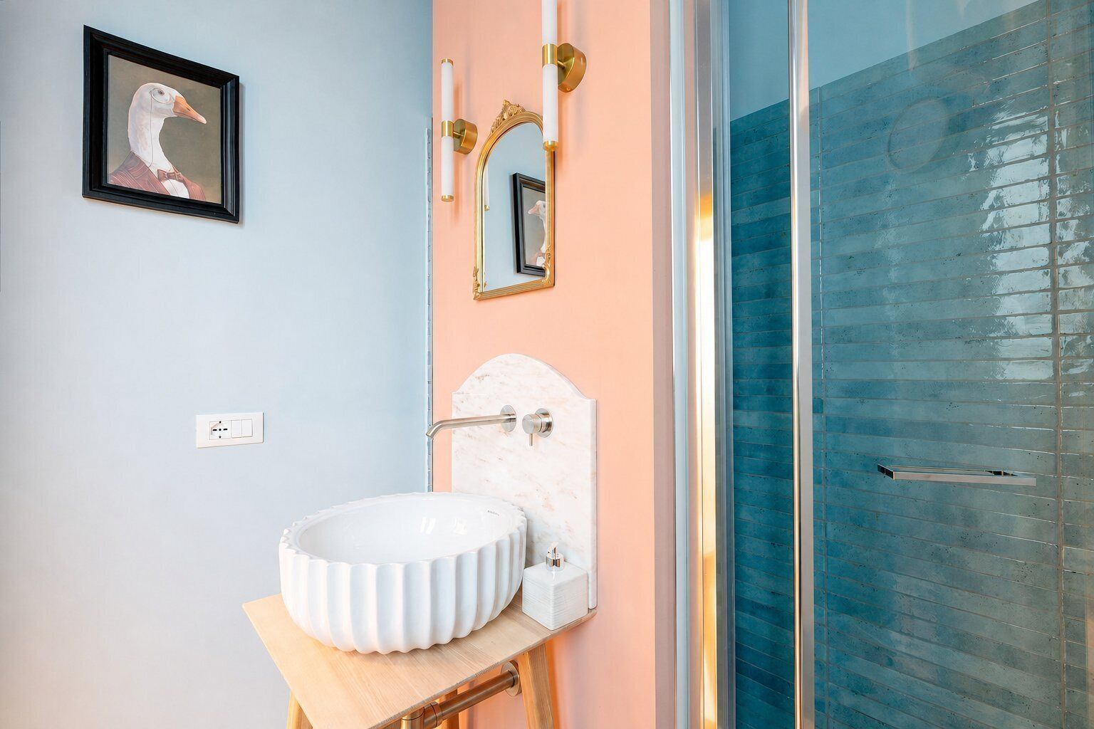 A bathroom with a white sink, a framed artwork, a mirror with gold accents, and a glass shower enclosure.