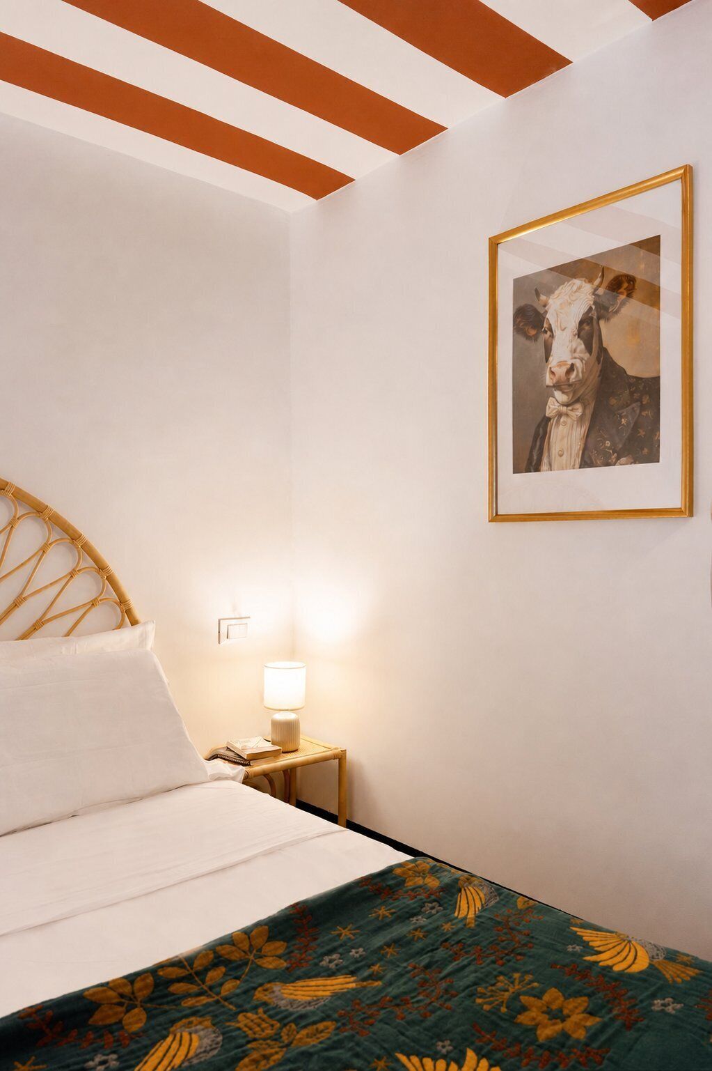 Een slaapkamer met een bed, nachtkastje, lamp en een ingelijst schilderij aan de muur.