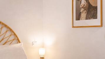 Een slaapkamer met een bed, nachtkastje, lamp en een ingelijst schilderij aan de muur.