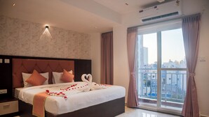 Ein modernes Hotelzimmer mit einem großen Bett, einer gepolsterten Kopfstütze und Blick auf die Stadt durch ein großes Fenster.