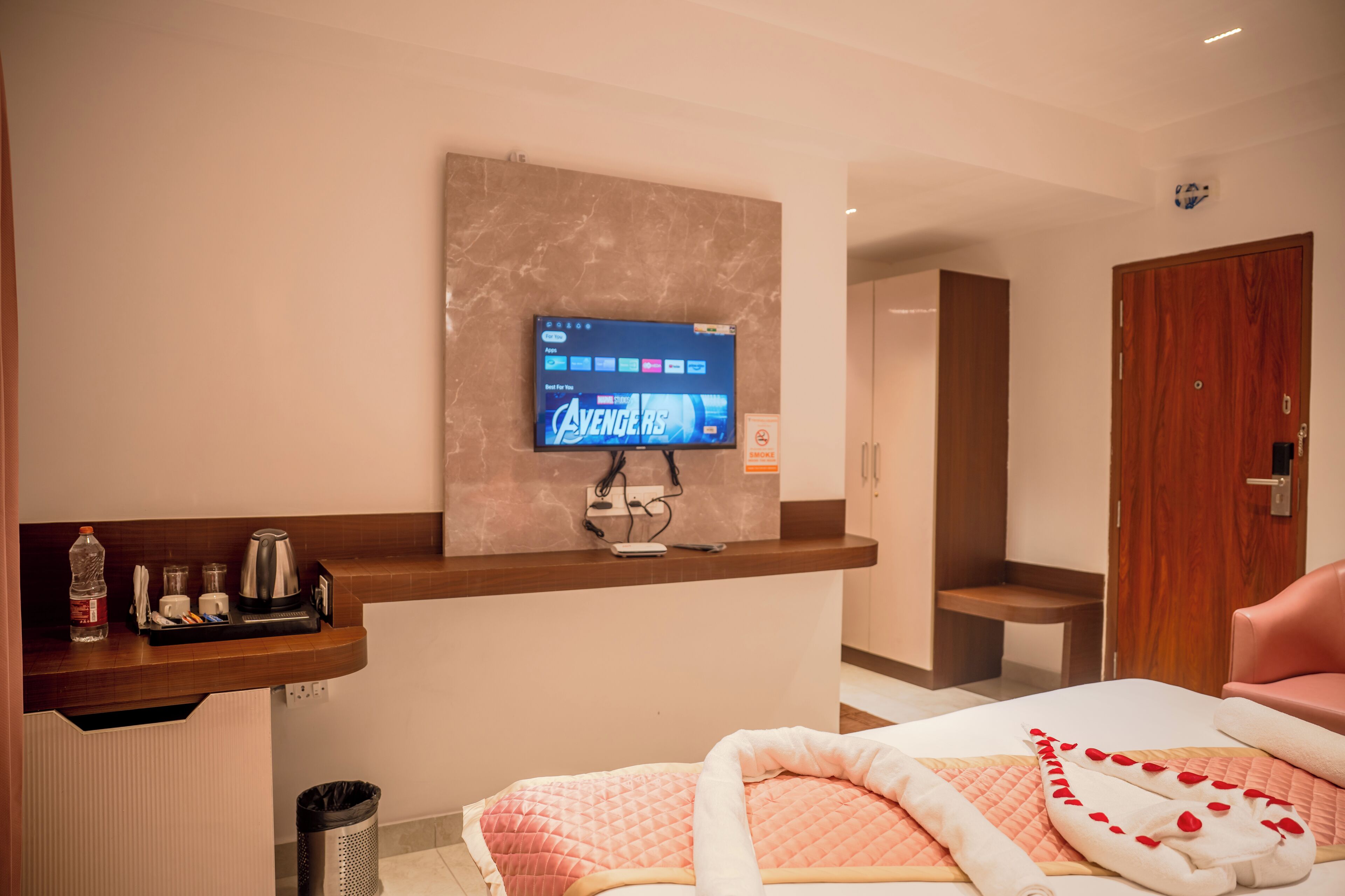 Een hotelkamer met een televisie aan de muur, een bed met een roze sprei, een houten bureau en een prullenbak.