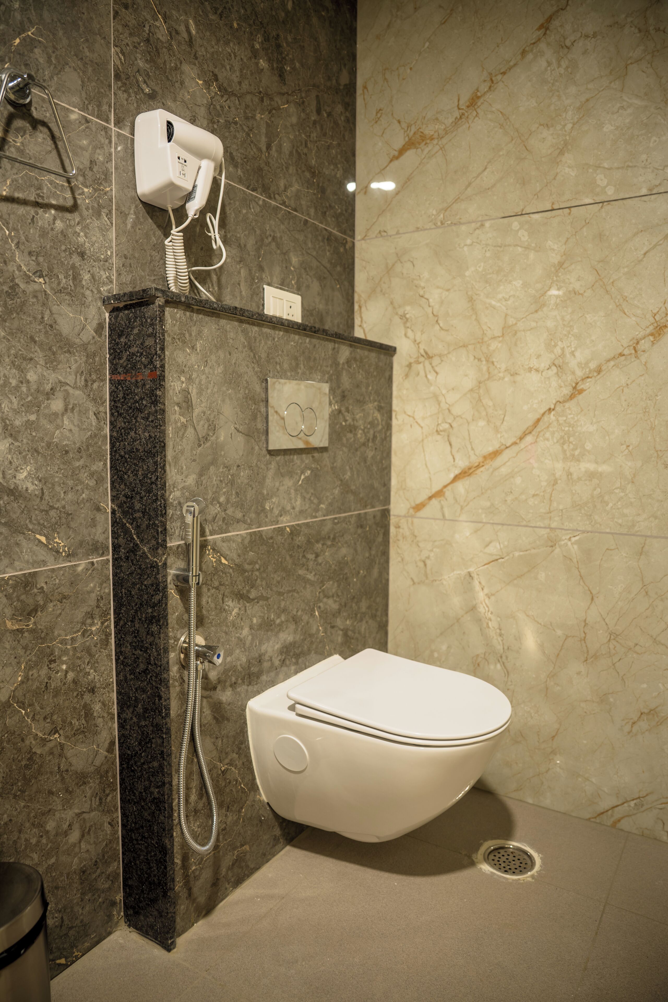 A bathroom with a marble wall, a toilet, a shower, and a hairdryer on the wall.