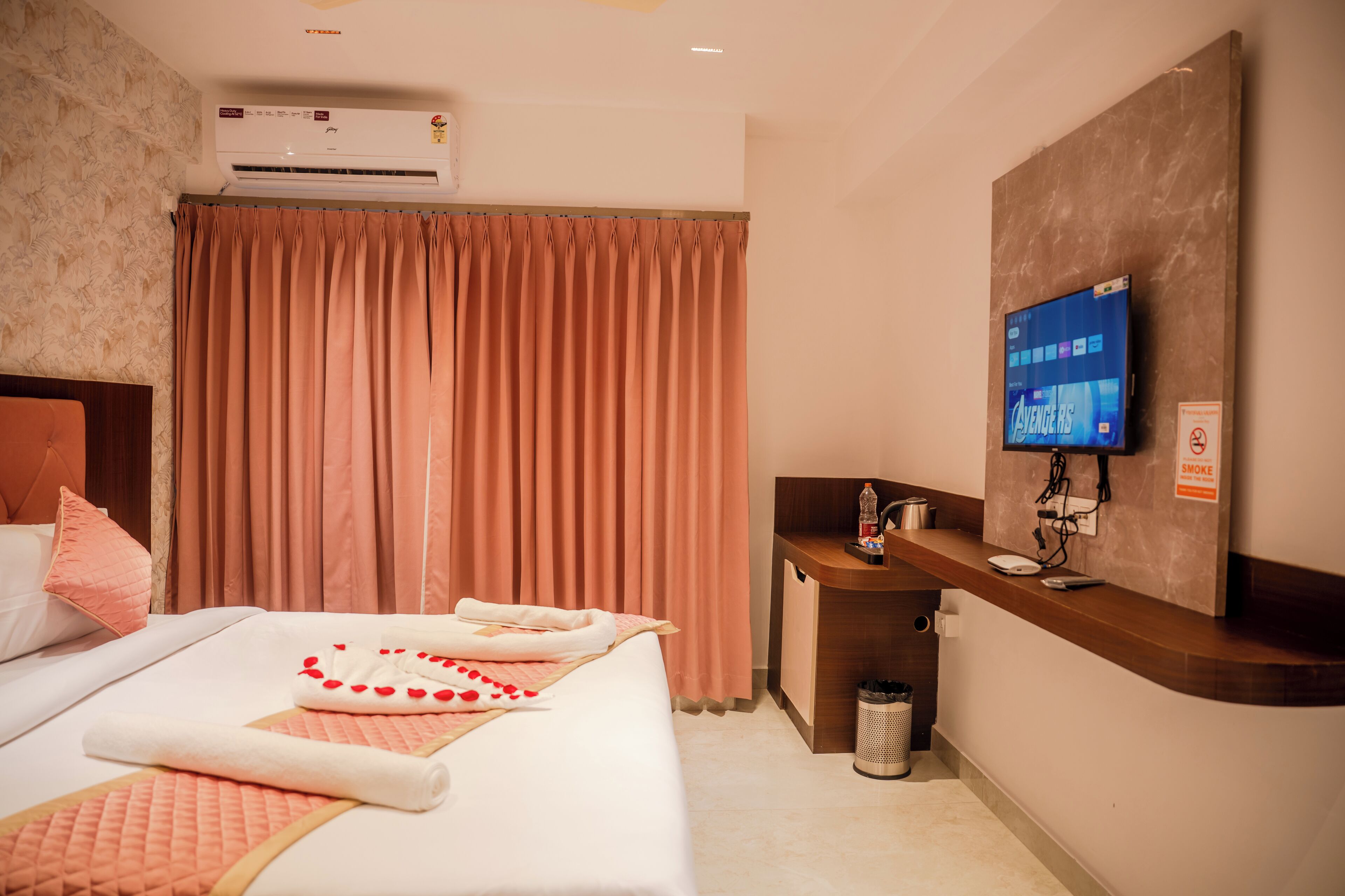 A hotel room with a bed, a desk, a television, and an air conditioning unit.