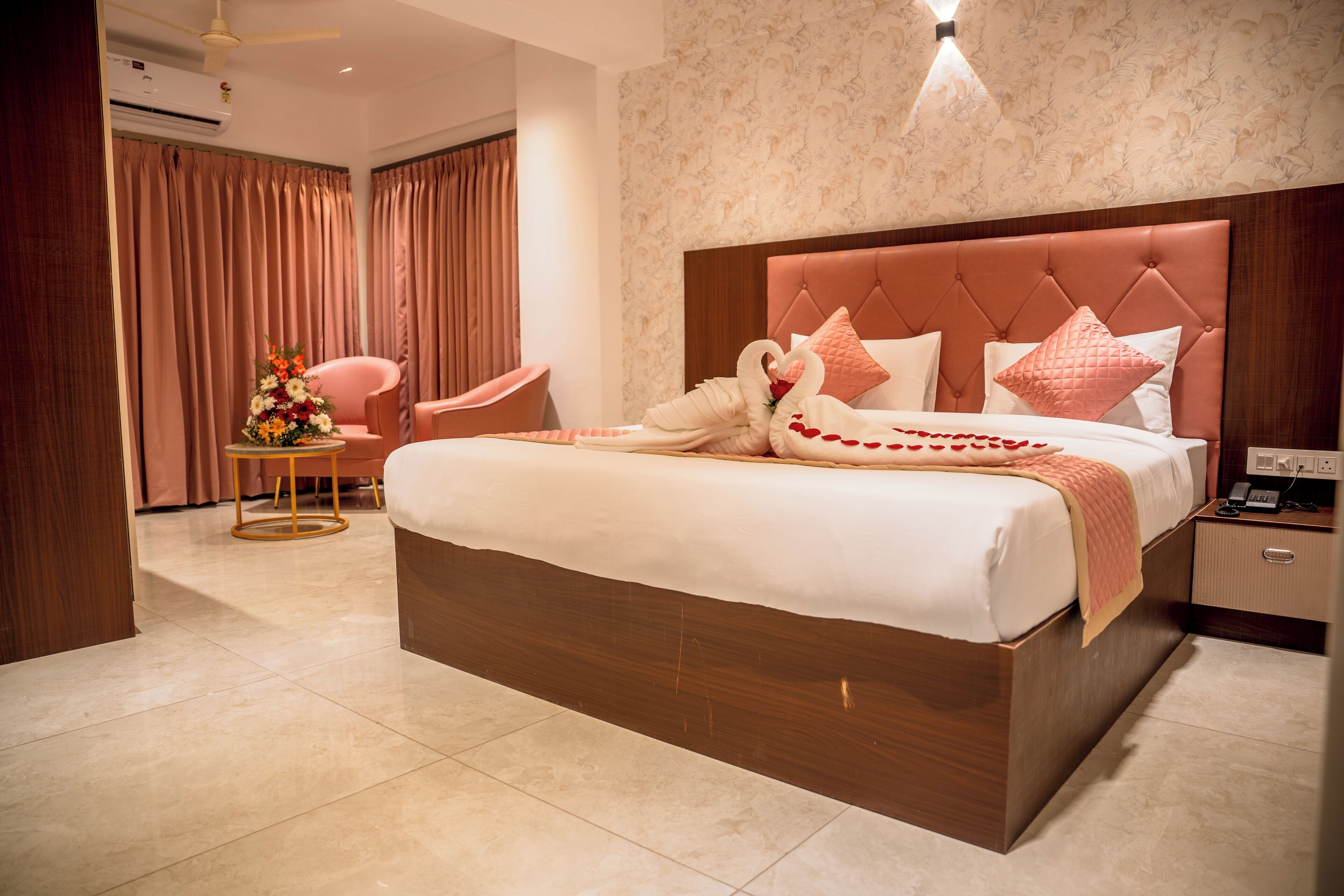 A spacious bedroom with a large bed, a sitting area with a chair and a small table, and a decorative swan arrangement on the bed.
