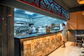 A commercial kitchen with a tiled backsplash and a counter where staff are preparing food.
