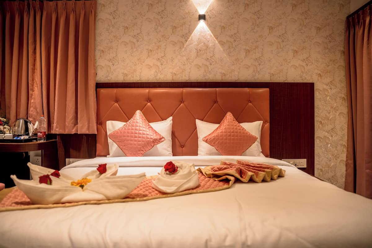 Una cama bien tendida con un cabecero rosa, una mesita de noche con una lámpara y un estampado de flores en el papel tapiz.