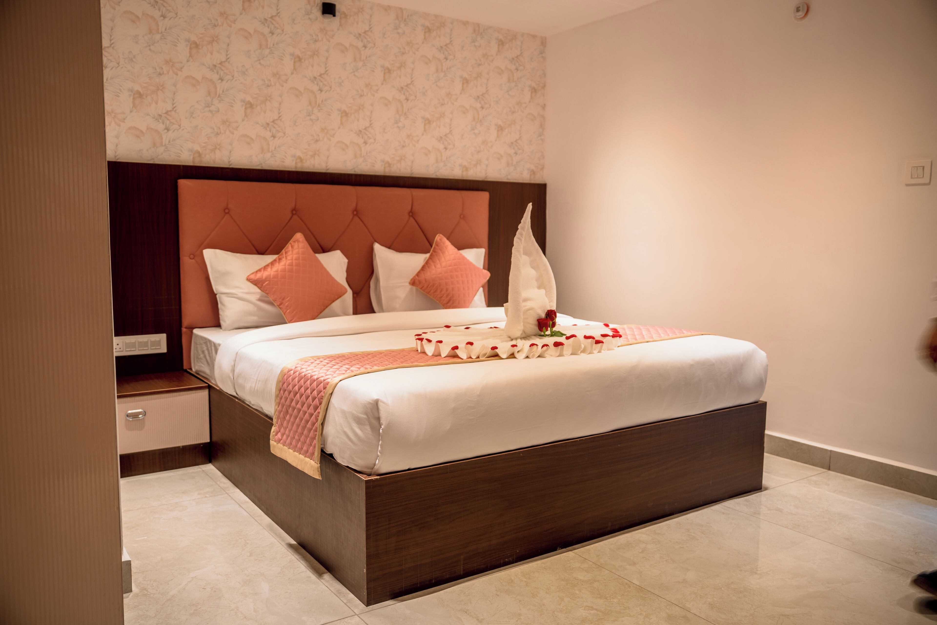 A neatly made bed with a wooden headboard, a bedside table, and a wall with a floral pattern.