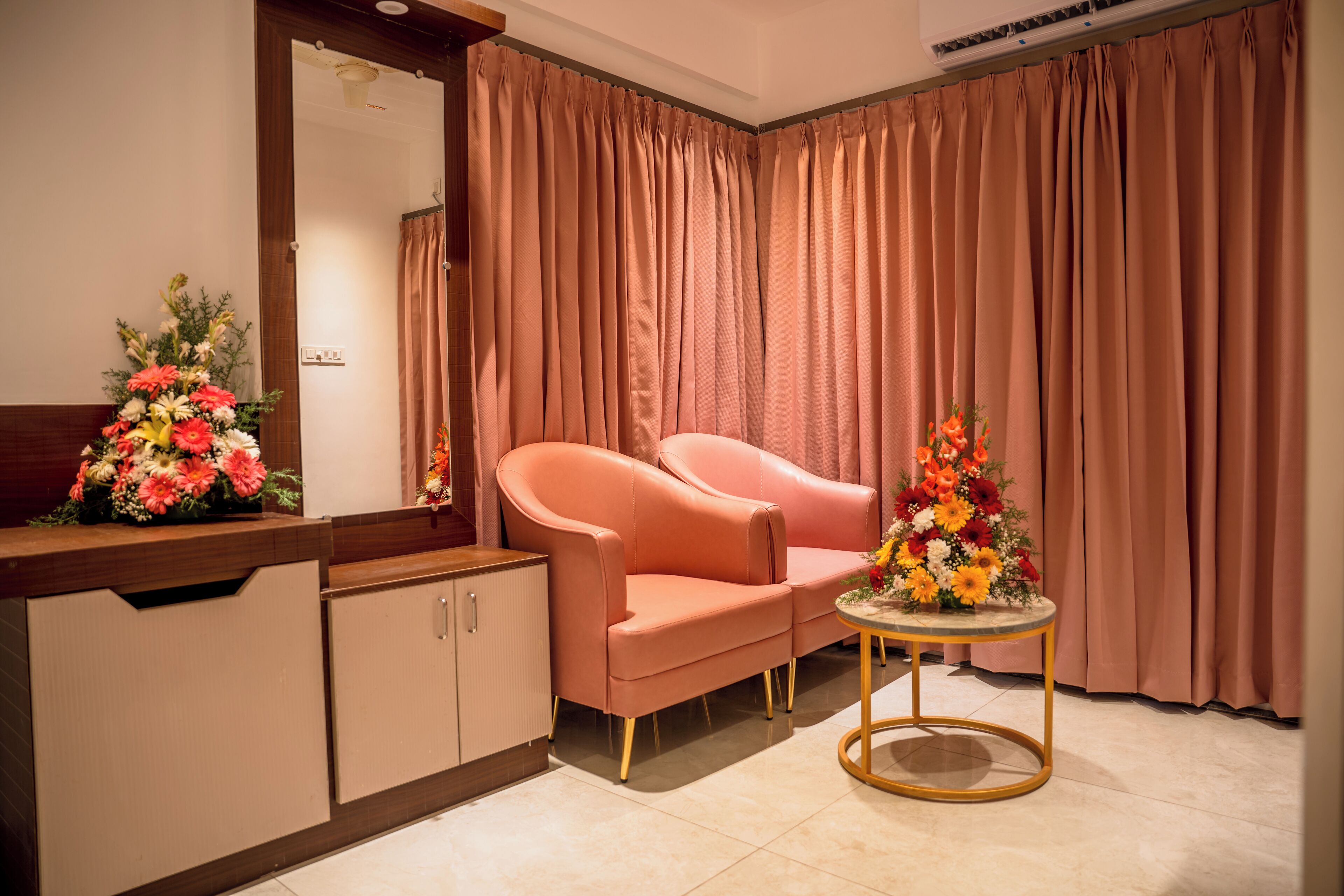 A room with a pink sofa, a small round table with a floral centerpiece, and a mirror above a wooden cabinet.