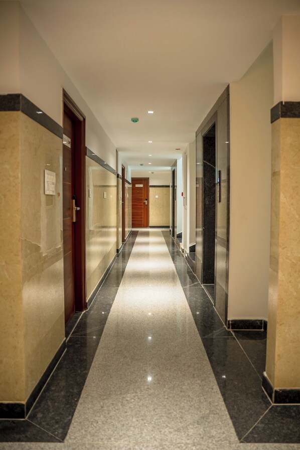 Un pasillo largo y estrecho con piso pulido, puertas a ambos lados y una puerta de madera al final.